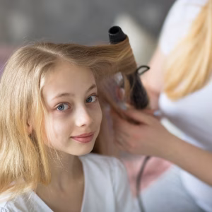 beautiful mother cares about a teenage daughter. Mom curls straightens hair to her daughter, Mom and daughter with long blond hair, concept of tenderness and care in real room